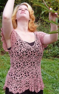 a woman is standing in the grass and reaching up to catch a frisbee