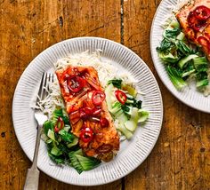 two white plates topped with meat and veggies on top of a wooden table