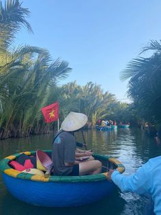 a person sitting in a small boat on the water near palm trees and other people