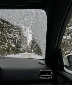 the inside view of a car driving down a snow covered road with trees on both sides