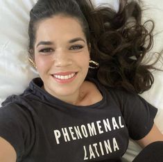 a woman laying in bed with her hair blowing in the wind and wearing a black shirt that says, phenomenal latina