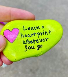 a hand holding a green rock with a pink heart on it that says leave a heartprint wherever you go