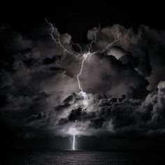 a lightning bolt is seen in the dark clouds above the ocean on a stormy night