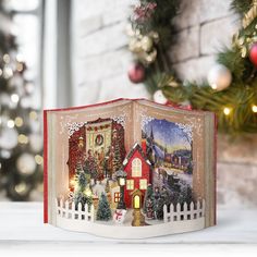 an open book with christmas scenes on it sitting in front of a decorated christmas tree