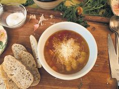 a bowl of soup and some bread on a cutting board next to utensils