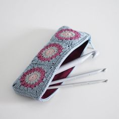 three crocheted pencils and two pens in a pouch on a white surface