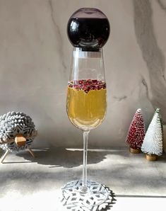 a glass filled with liquid sitting on top of a table next to small christmas trees