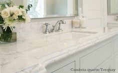 a bathroom with marble counter tops and white flowers in a glass vase on the sink