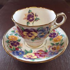 a cup and saucer with flowers painted on the side sitting on a wooden table