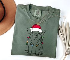 Spread holiday cheer with our Colorful Christmas Pig Tee! This vibrant shirt showcases a charming Pig adorned with a Santa hat and wrapped in colorful Christmas lights, making it a delightful gift for Pig moms and animal lovers. Crafted from comfortable, durable material, it's perfect for festive gatherings, holiday walks, or everyday wear during the season. Whether you're celebrating with family or gifting to a special Pig lover, this Cute Pig Shirt adds a touch of festive joy and warmth to any wardrobe. Celebrate with love and laughter! PRODUCT DESCRIPTION: Comfort Colors presents the "Comfort Colors 1717" t-shirt, a customizable, 100% ring-spun cotton garment. Soft-washed and garment-dyed, this relaxed-fit tee offers coziness and durability with double-needle stitching and seamless cons Colorful Christmas Lights, Pig Shirt, Pig Shirts, Cute Pig, Pig Lovers, Colorful Christmas, Cute Pigs, Animal Lovers, Santa Hat