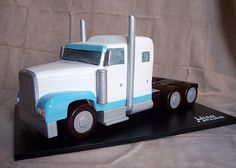 a cake shaped like a semi truck on a black base with white and blue trim