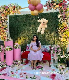 a pregnant woman sitting on a couch in front of a backdrop with flowers and balloons