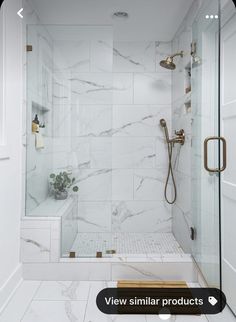 a walk in shower sitting next to a white tiled wall and floor with gold fixtures