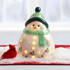 a snowman figurine sitting on top of a red table cloth next to a cardinal