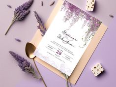 a purple and white wedding card on top of a table next to some lavender flowers