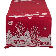 a red table runner with white snowflakes and houses on the front, along with pom - poms