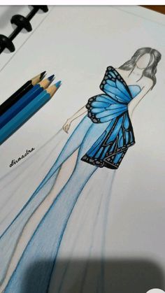 a drawing of a woman in a blue dress with butterfly wings on her back, next to colored pencils