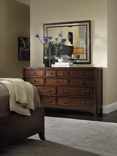 a bedroom scene with focus on the dresser and flowers in front of the large mirror