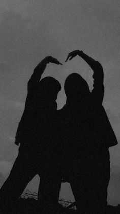 two people making a heart shape with their hands in the air while standing next to each other