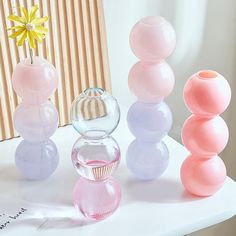 three vases with different colors and shapes on a white table next to a yellow flower