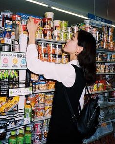 a woman is reaching for canned food in a grocery store she is looking up at the shelves