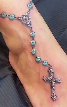 a woman's foot with a rosary and cross tattoo on the side of her leg