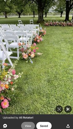 rows of white chairs with flowers on the grass in front of them and trees behind them