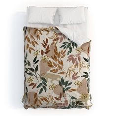 a bed covered in a white comforter next to a pillow with leaves on it