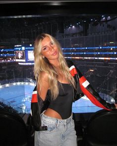 a beautiful young blond woman standing in front of a hockey rink