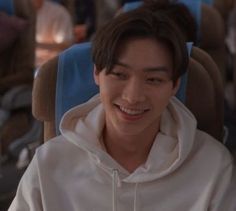 a young man sitting in a chair with his eyes closed and wearing a white hoodie