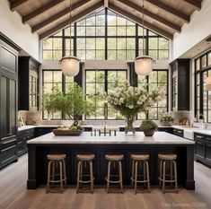 a large kitchen with black cabinets and white counter tops, an island in the center is flanked by stools