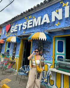 a woman standing in front of a blue building with yellow and white awnings