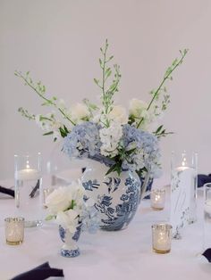 a vase filled with white and blue flowers sitting on top of a table next to candles