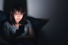 a woman sitting in bed looking at her cell phone with the light shining on her