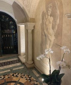 a vase with flowers in it sitting on the floor next to a wall that has an angel painting on it