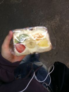 someone is holding up a sandwich with fruit on it in their hand and ear buds attached to the bag