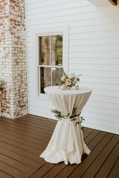 a white table with flowers on it sitting in front of a brick wall next to a window