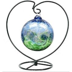 a heart shaped sculpture with a green and blue swirl on it's base, hanging from a black metal stand