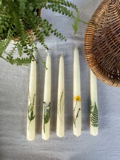 four white candles with plants on them next to a basket