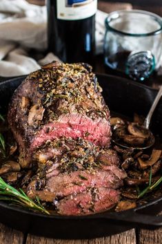 steak with mushrooms in a cast iron skillet next to a bottle of red wine