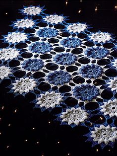 a blue and white crocheted doily with stars in the center on a black background