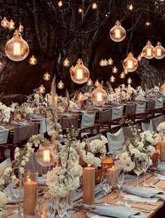 an outdoor dining area with candles and flowers on the table, surrounded by hanging lights