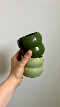 a hand is holding three green bowls in each other's hands, with one being held up by the other