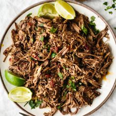 shredded pork with limes and cilantro on a plate next to a fork