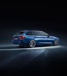 the rear end of a blue bmw car in a dark room with its lights on