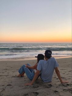 a man and woman sitting on the beach watching the sun go down over the ocean