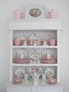 a white china cabinet with dishes and cups on top of it, all decorated in pink