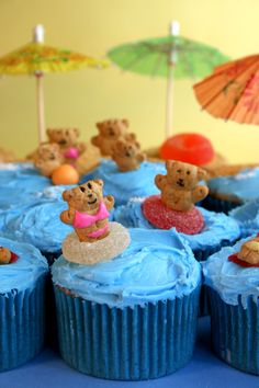 cupcakes with blue frosting and teddy bears in the sand on top are decorated with beach - themed cakes