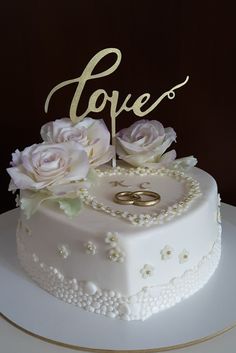 a wedding cake with two rings and flowers on top that says love in gold lettering