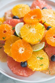 grapefruit, oranges and blueberries are on a white plate with lime